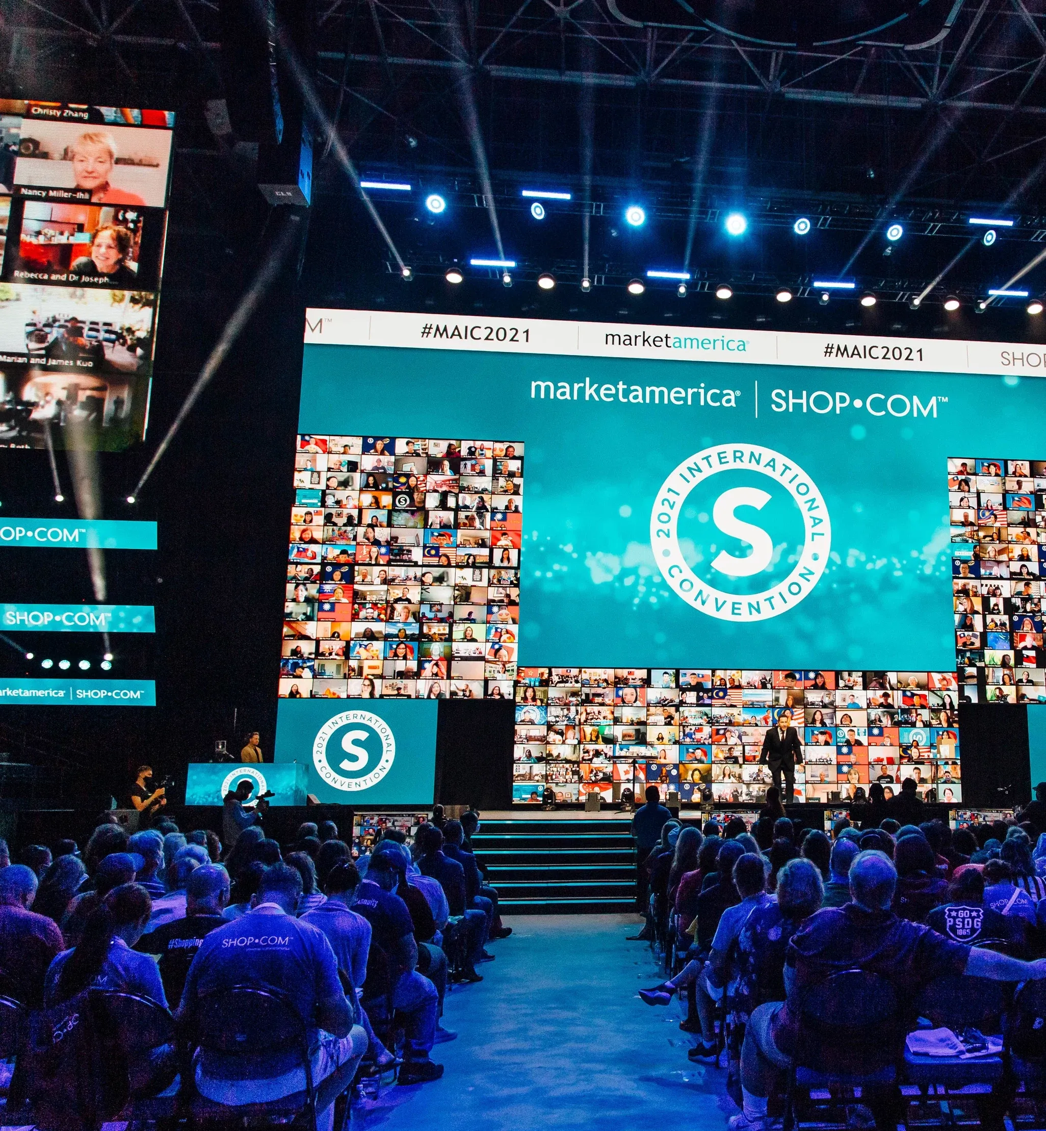 Seated audience faces a Market America stage with a 2021 International Convention logo and walls of virtual attendees