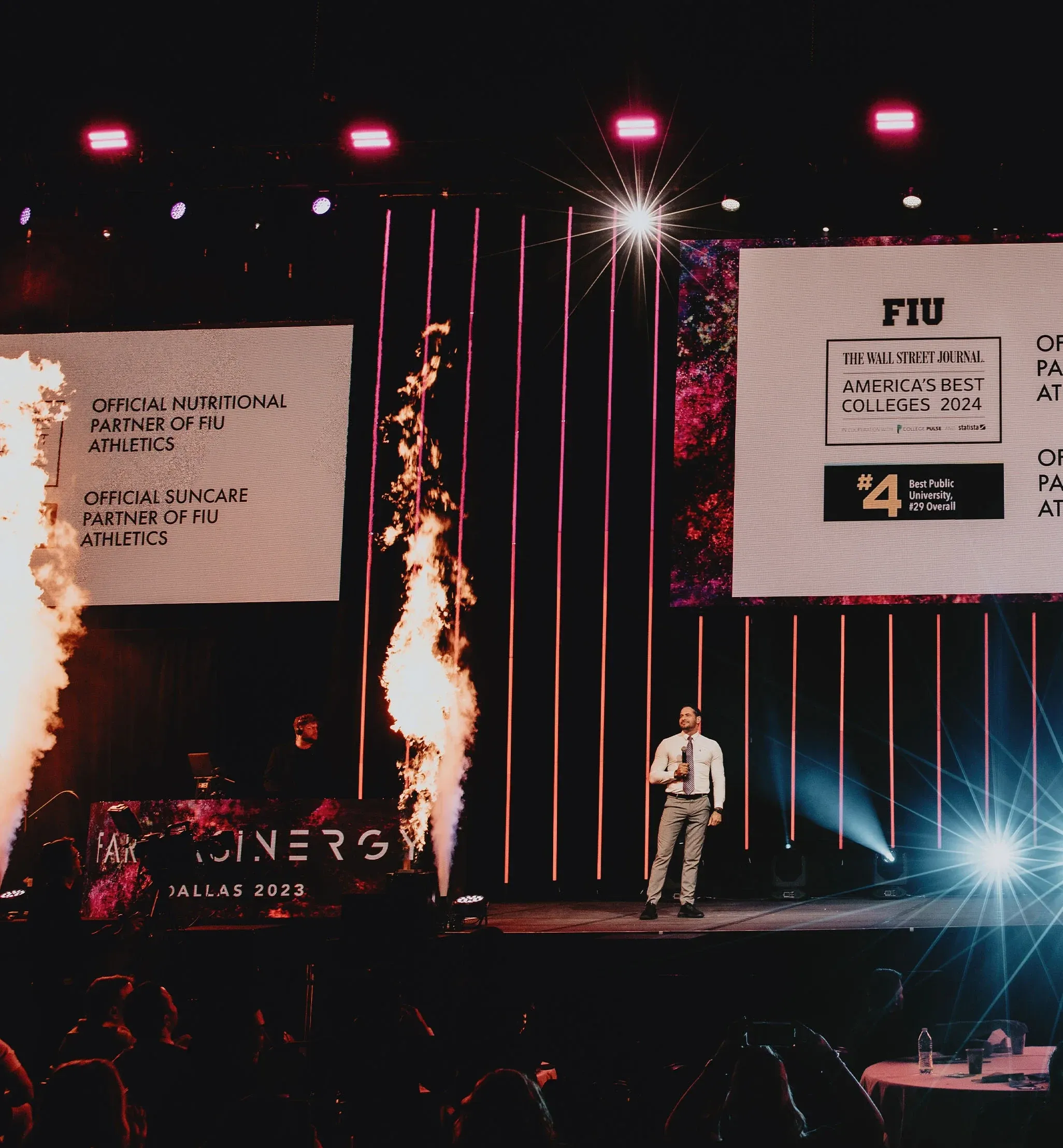 Presenter on the Farmasinergy Dallas 2023 stage as flame effects fire beside partnership slides