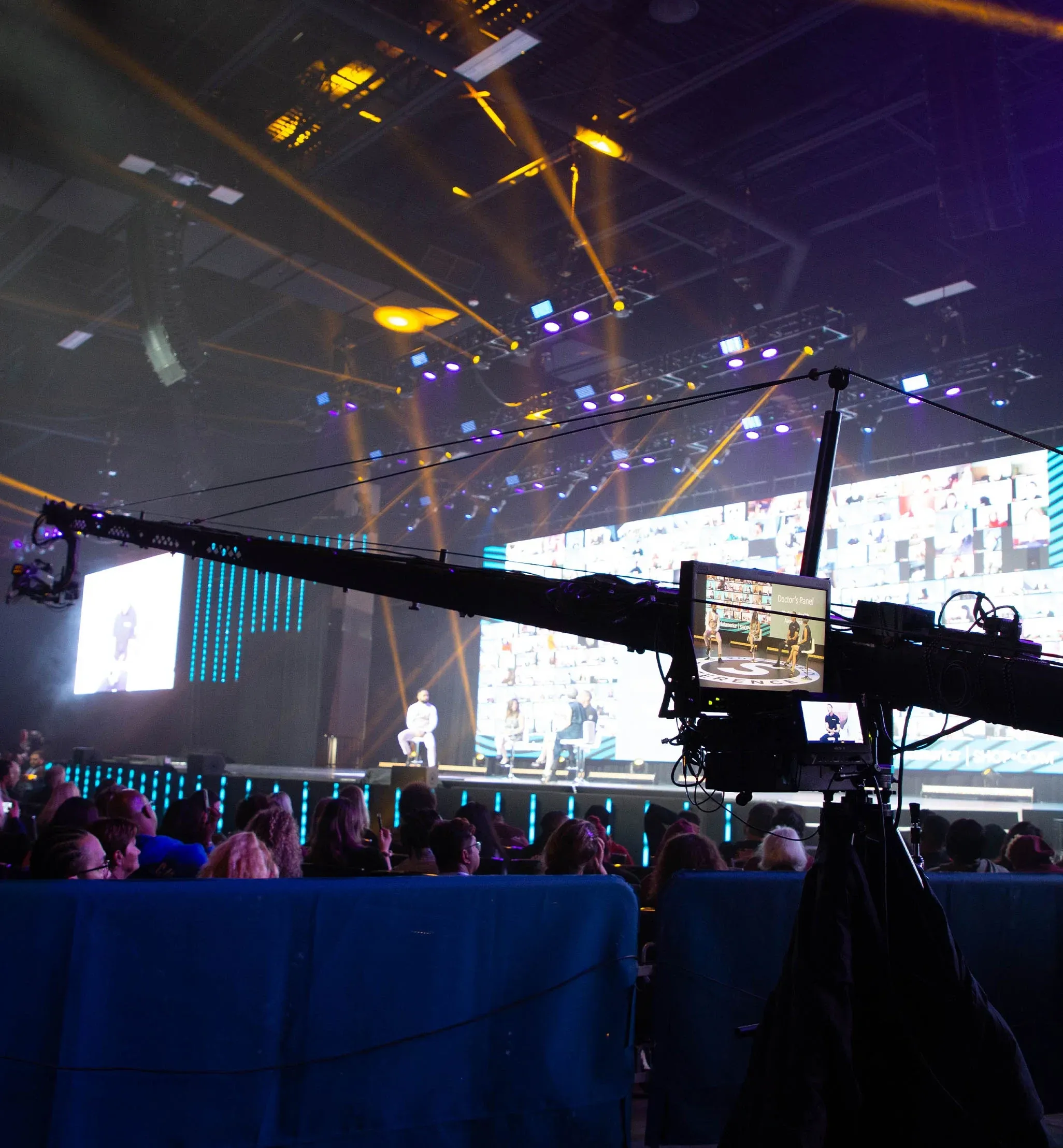 Camera jib with monitor showing a Doctor's Panel arcs over the audience toward a stage of virtual attendees