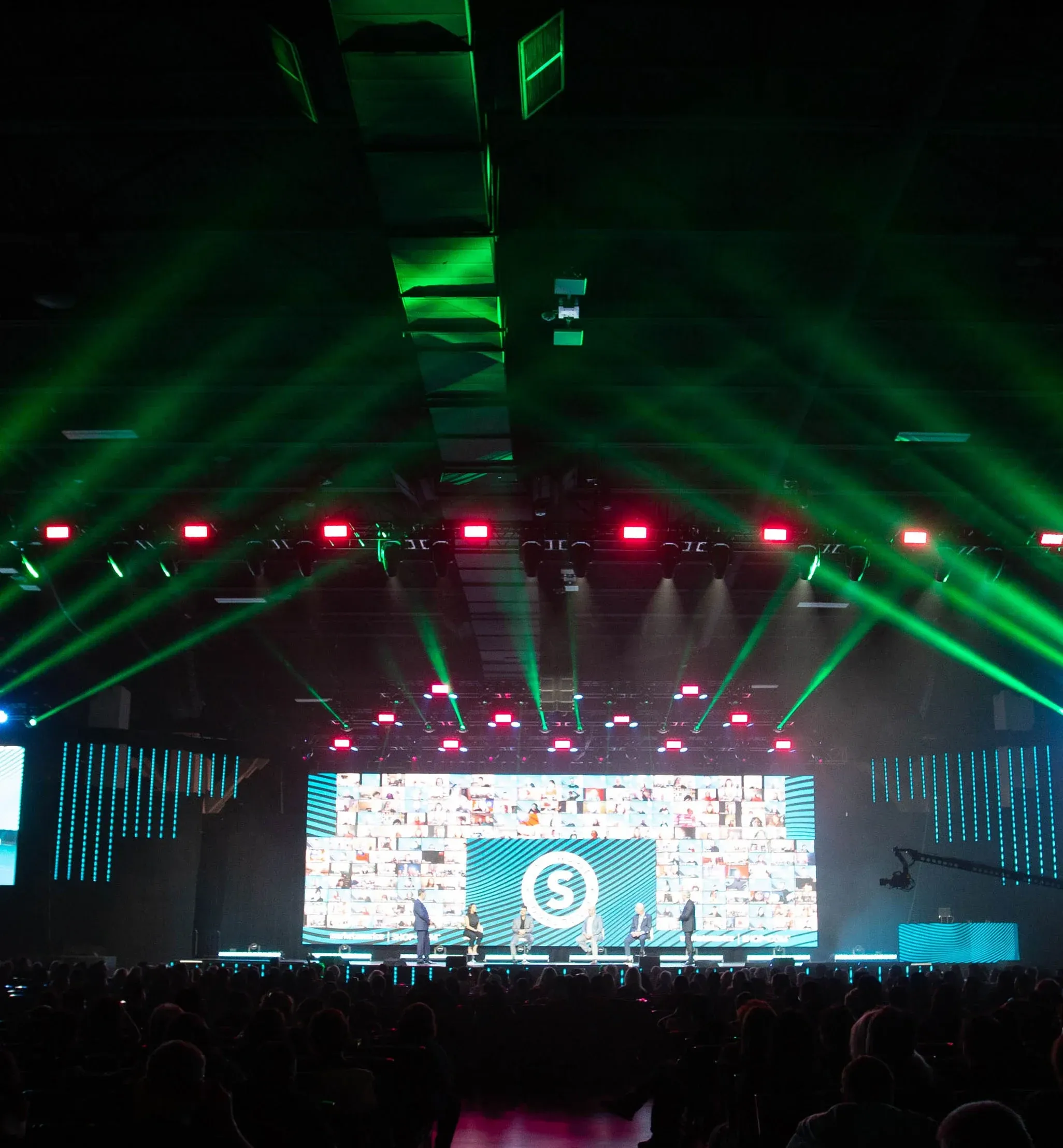 Green beam lights fan above a dark hall as a panel sits before a Market America virtual-attendee wall