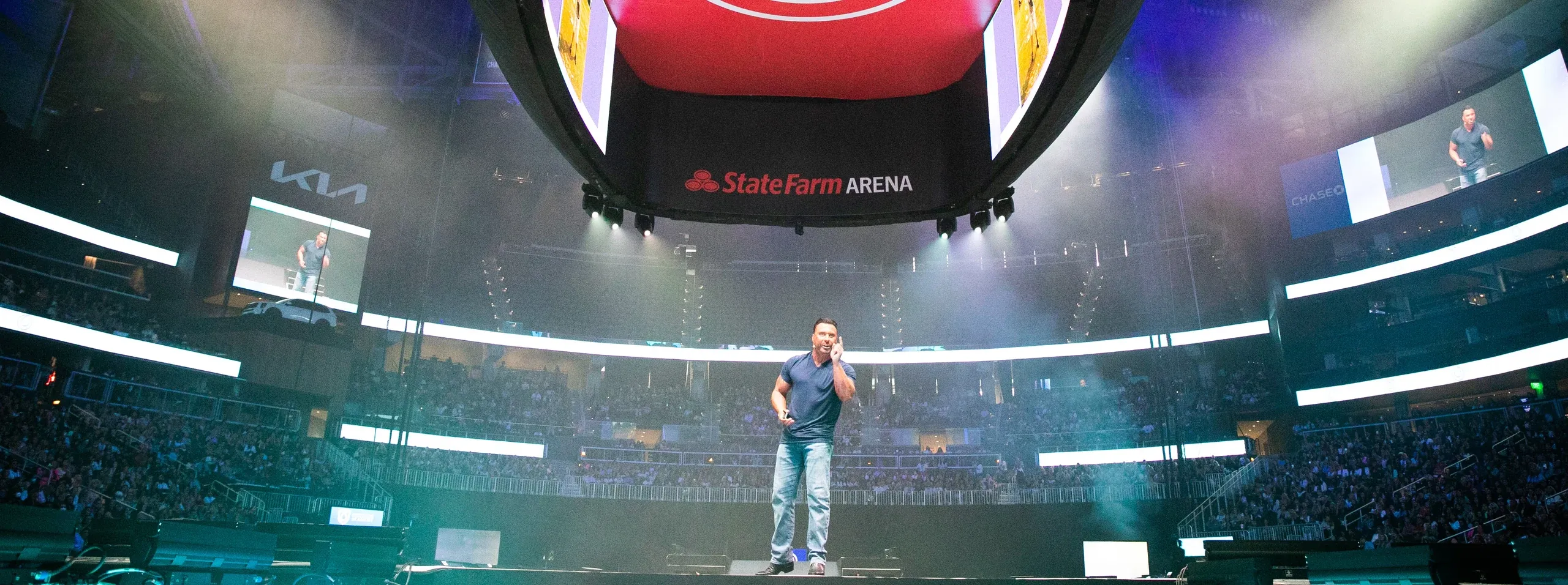 Speaker on a center stage beneath the State Farm Arena scoreboard with IMAG screens and filled stands