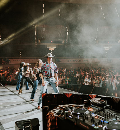 dj wearing black leather jacket with arms raised to crowd in a spotlight