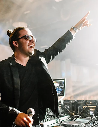 dj wearing black leather jacket with arms raised to crowd in a spotlight